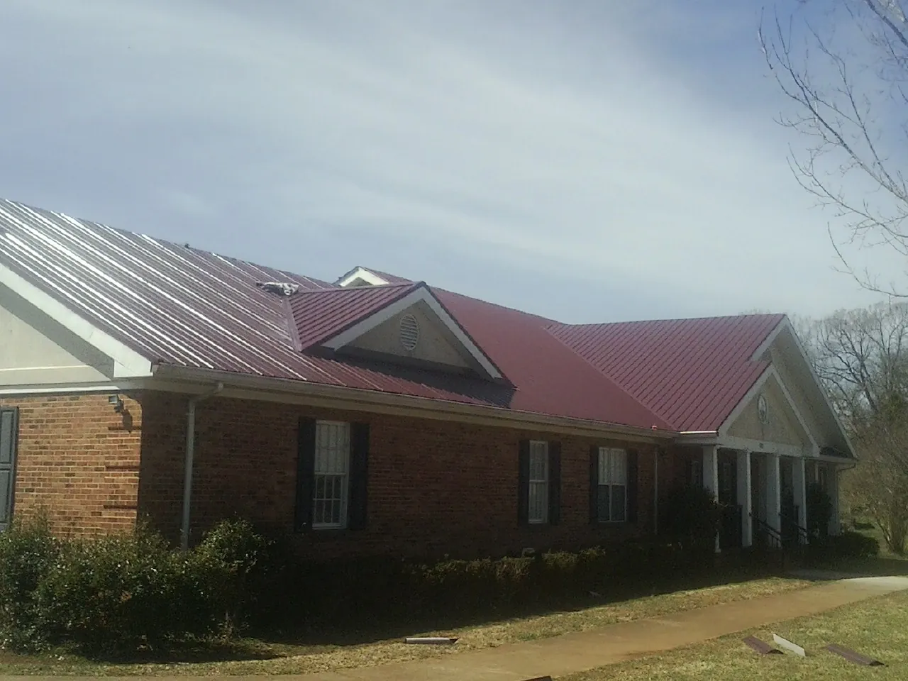 Red metal roof with gabled entries on a long brick building, from a Hail Damage Roof Repair job in Thetford Center