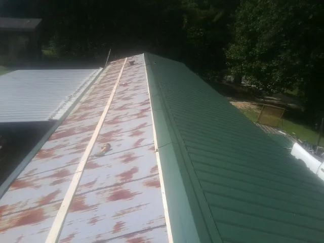 Old rusted panels beside newly installed green metal roofing — Wind Damage Roof Repair by Roofing Brothers in Thetford Center