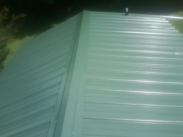 New green metal panels meeting at the ridge of a roof — Flat Roof Repair work by our crew in Thetford Center