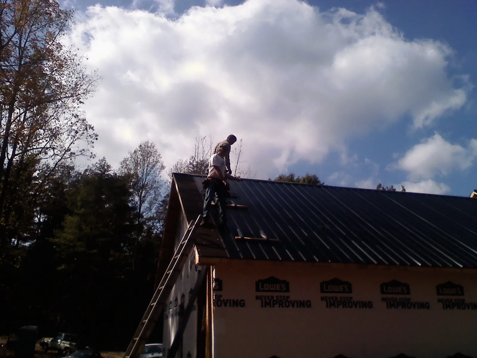 Roofer fastening dark metal panels high against a cloudy sky, from a Roof Inspection job in Thetford Center