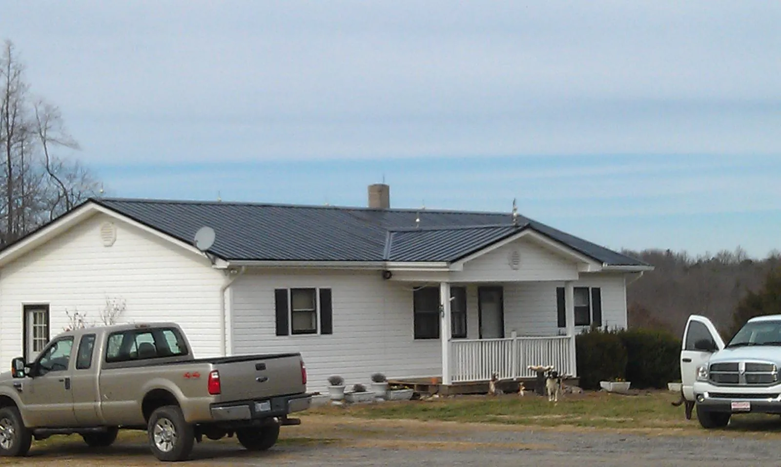 Finished dark metal roof on a white ranch home with work trucks parked in Thetford Center