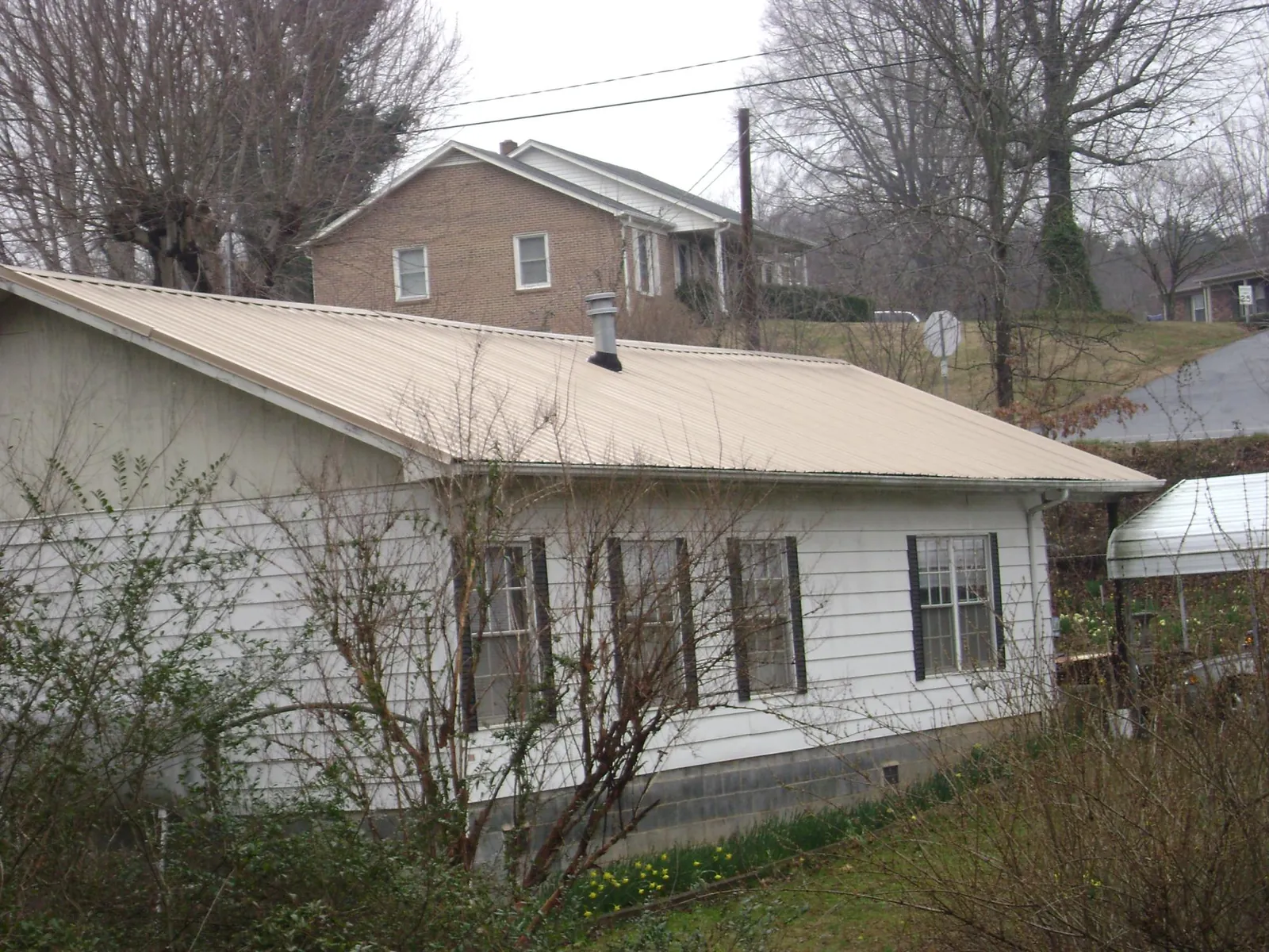 Tan metal roof on a white sided house set into a hillside — Commercial Roofing by Roofing Brothers in Thetford Center